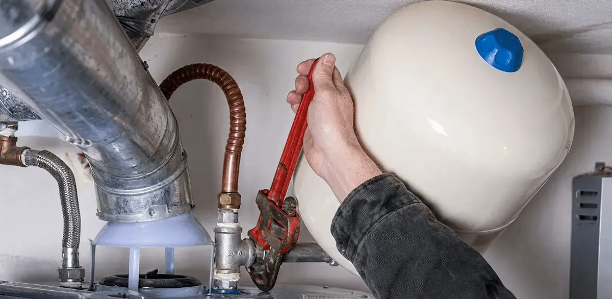 Water heater repair technician tightening plumbing connections near a tank unit in South Bend, IN